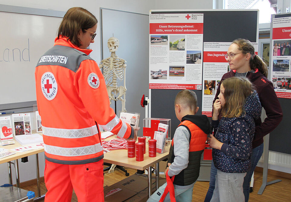 Eine Frau und zwei Kinder schauen auf den Tisch eines Infostandes, eine Frau in Einsatzkleidung steht daneben
