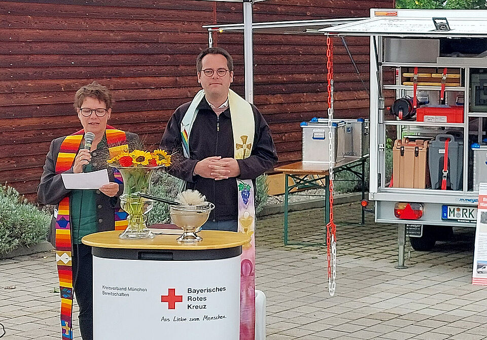 Ein Mann und eine Frau stehen hinter einem Rednerpult mit Rotkreuzlogo