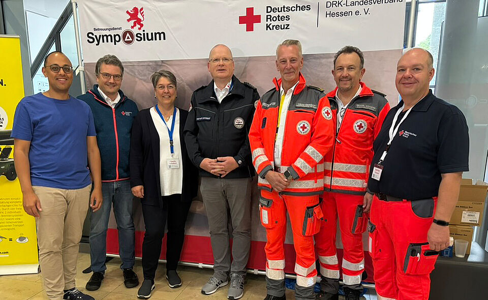 7 Rotkreuzler*innen stehen als Gruppe vor einer Fotowand