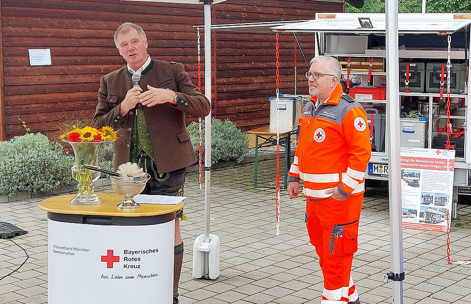 Eine Person steht an einem Rednerpult, eine Person in Einsatzkleidung steht dahinter